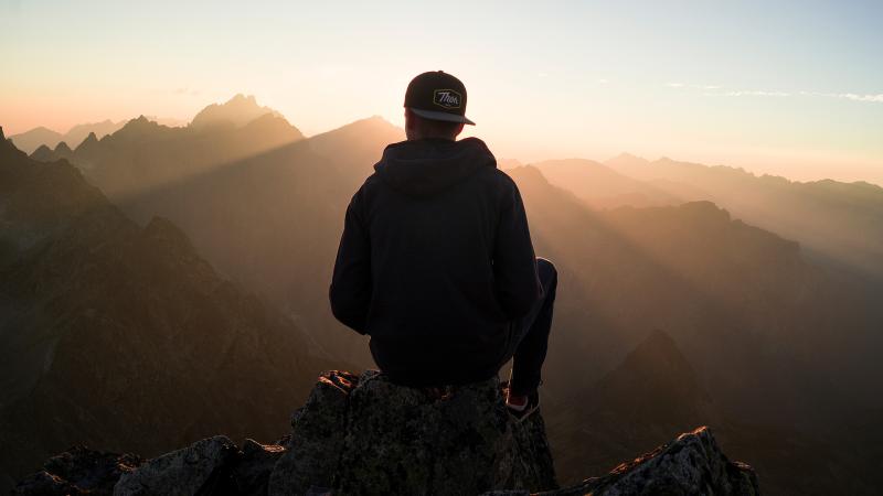 Man With Cap Sitting On The Mountain Edge