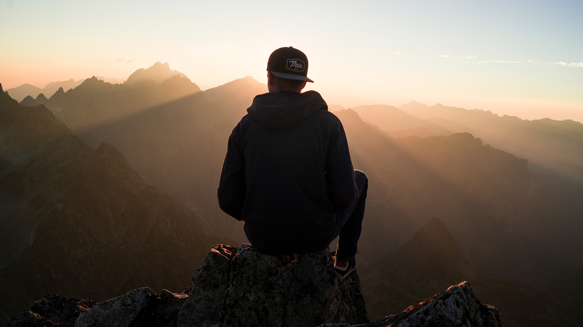 Man With Cap Sitting On The Mountain Edge