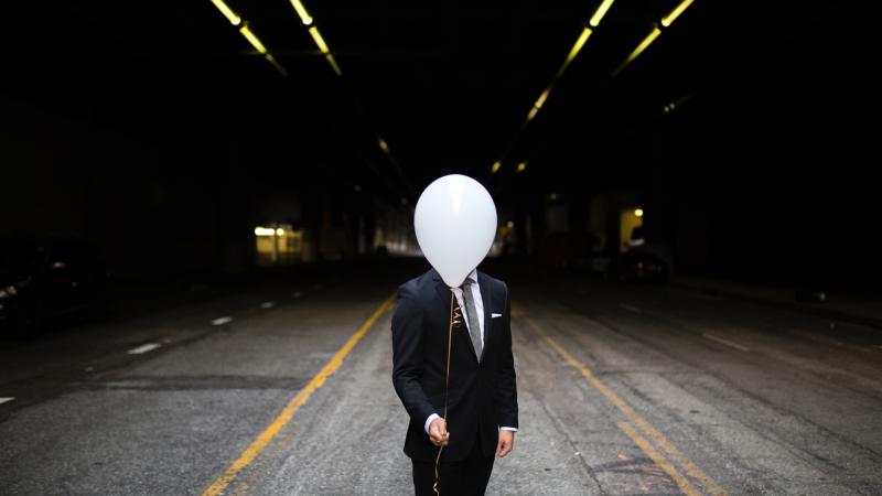 Young Man In Suit Holding Balloons In Front Of Face